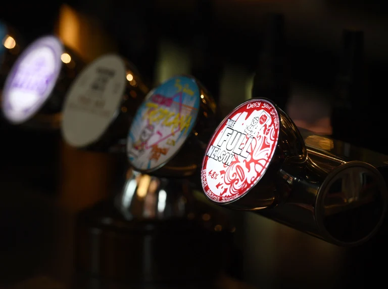 Rhes o dapiau cwrw lliwgar mewn bar.
