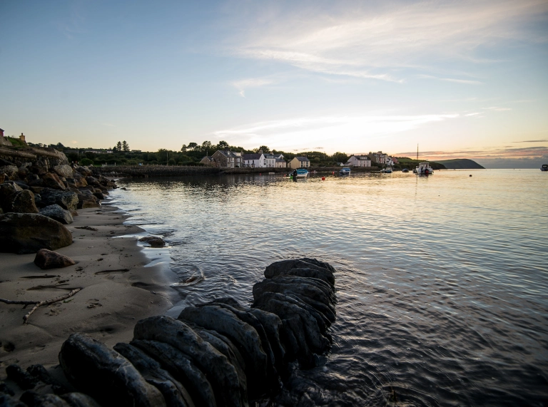 Glan y môr gyda thai yn y cefndir wrth iddi fachlud
