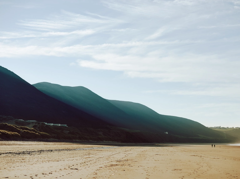Traeth tywodlyd gyda bryniau yn y cefndir
