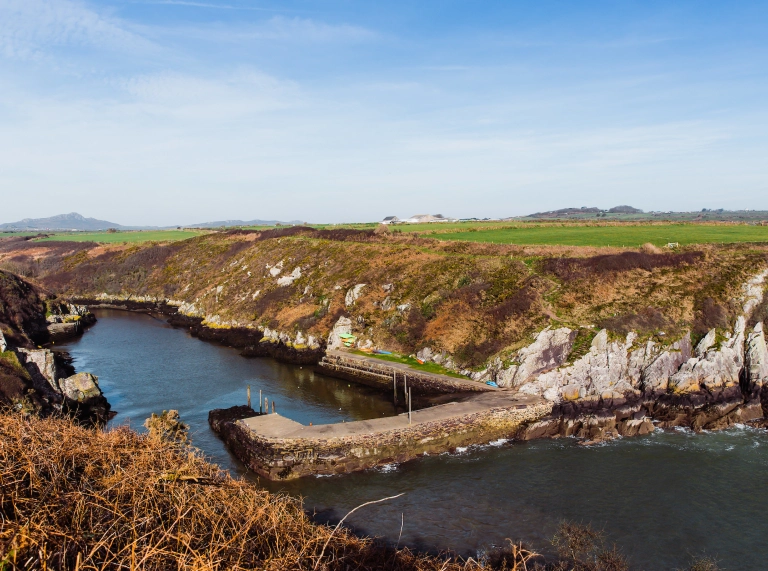 Harbwr bach wedi’i amgylchynu gan glogwyni a’r llanw i mewn.