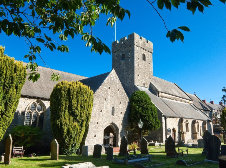 Golygfa allanol o Eglwys Sant Illtyd gydag awyr las a beddau y tu allan