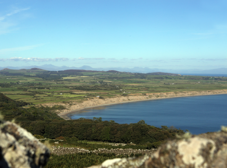 Golygfa o'r môr gyda chaeau gwyrdd o amgylch