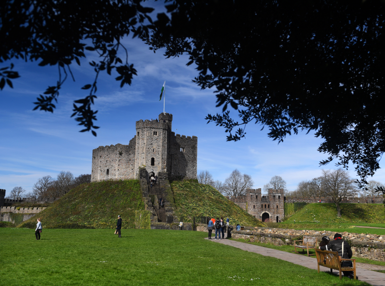 People walking up to The Keep, a tower at Cardiff Castle framed by a tree in the foreground.