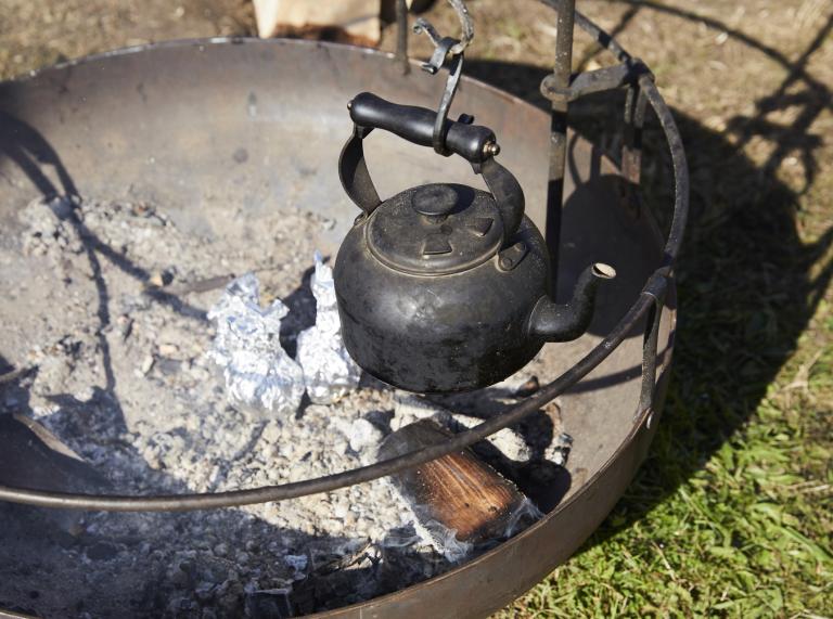 A metal kettle hanging over a fire pit.