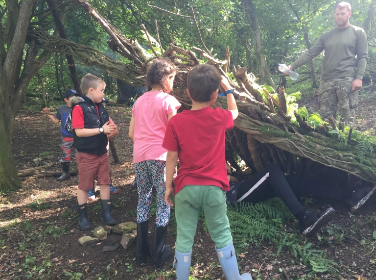 Plant yn adeiladu den gyda choed.