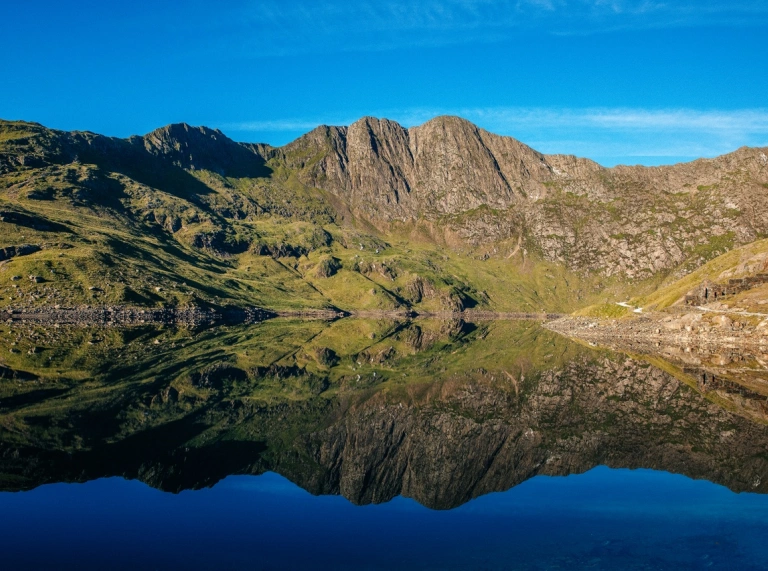 Llyn Llydaw ar ddiwrnod heulog gyda' Wyddfa yn y cefndir ac wedi'i adlewyrchu yn y dŵr.
