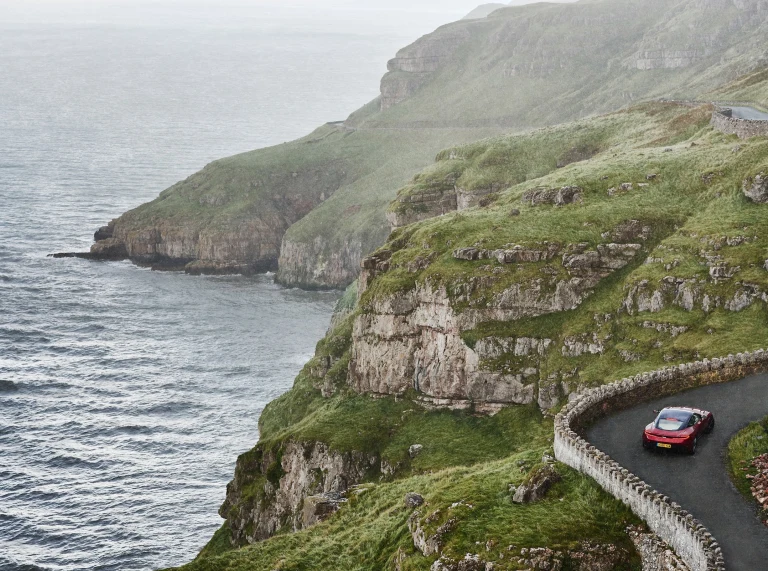 Car yn gyrru ar hyd ffordd droellog gyda'r môr ar yr ochr chwith