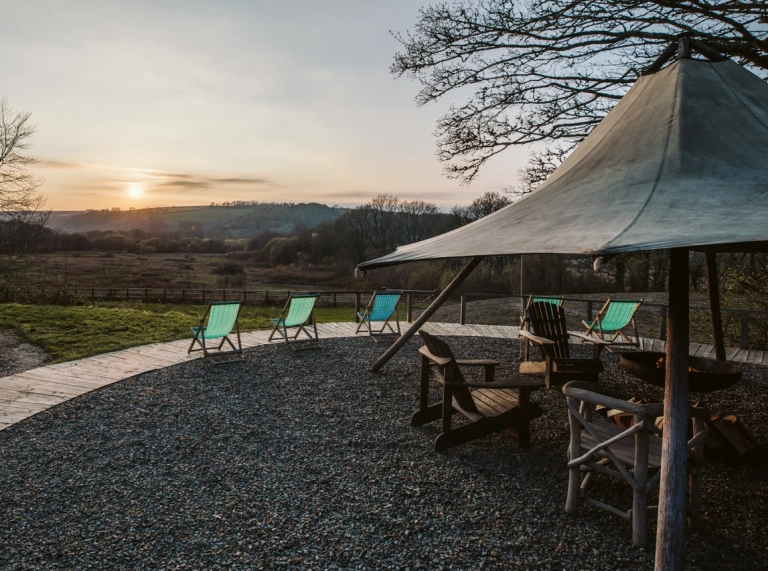 Tipi a chadeiriau gyda bryniau a machlud haul mewn pellter.