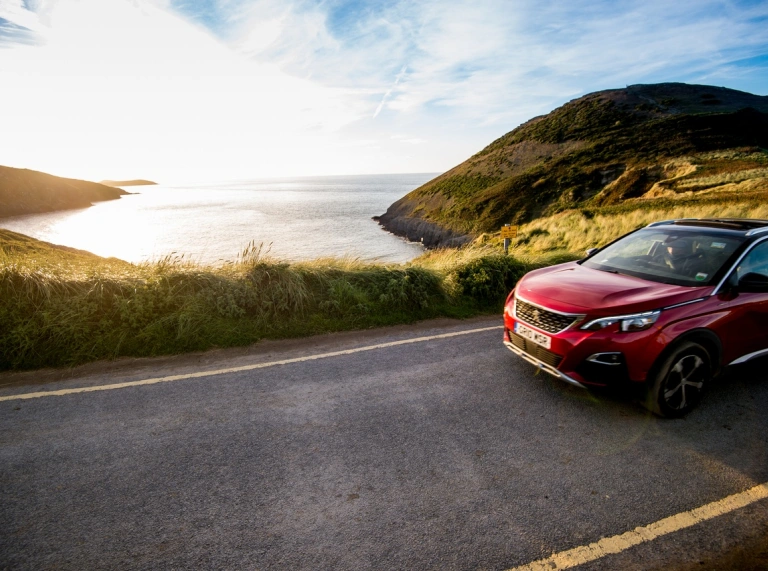 Car coch yn gyrru ar ffordd sy'n edrych dros y môr