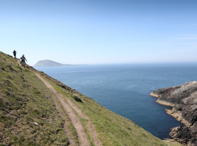 Cwpwl yn cerdded ar hyd Llwybr Arfordir Cymru gyda'r môr ar yr ochr dde