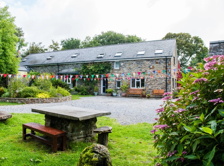 Adeiladu yn Mandala Ashram gyda baneri lliwgar a mainc bicnic y tu allan