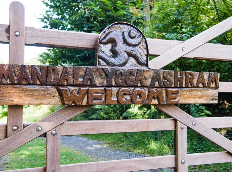 Giât bren gydag arwydd cerfiedig 'Mandala Yoga Ashram Welcome'