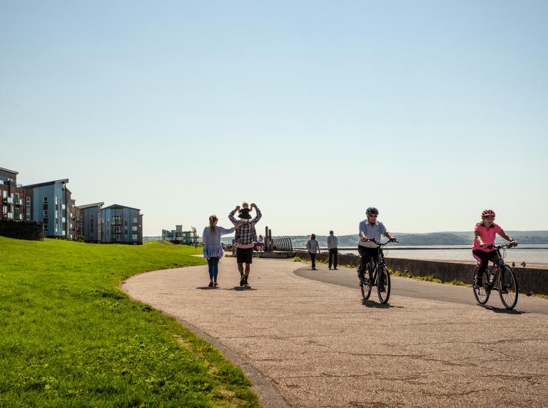 people walking and cycling along coastal walkway.