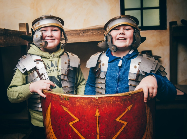 Dau wedi gwisgo fel milwyr Rhufeinig yn dal tarian.