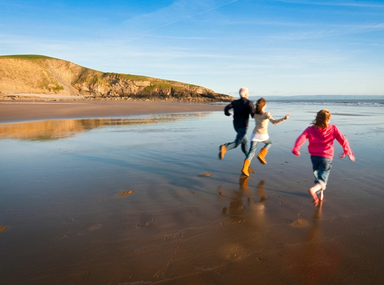 Llun o deulu'n rhedeg ar y traeth