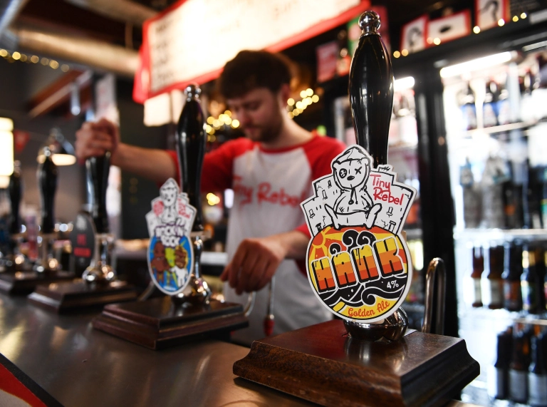 Barman yn tynnu peint a tapiau cwrw lliwgar ar y bar pren.