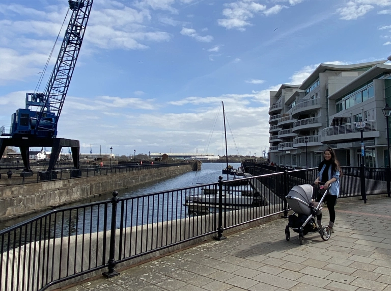 Menyw a phram yn cerdded ym Mae Caerdydd