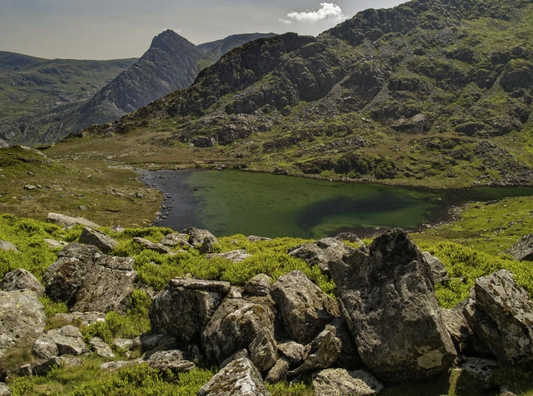 Llyn rhewlifol islaw mynyddoedd gwyllt.