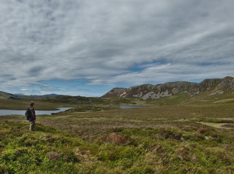Dyn â gwialen bysgota ger llyn.