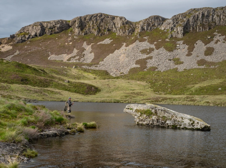 Dyn yn pysgota plu mewn llyn.