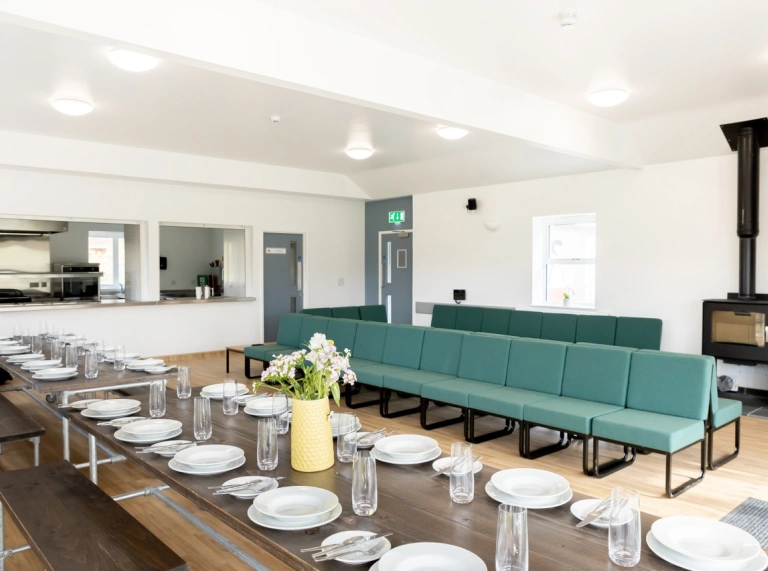 Glan-llyn Isa’s large communal room with a dining table that can seat a crowd and a comfortable green sofa.
