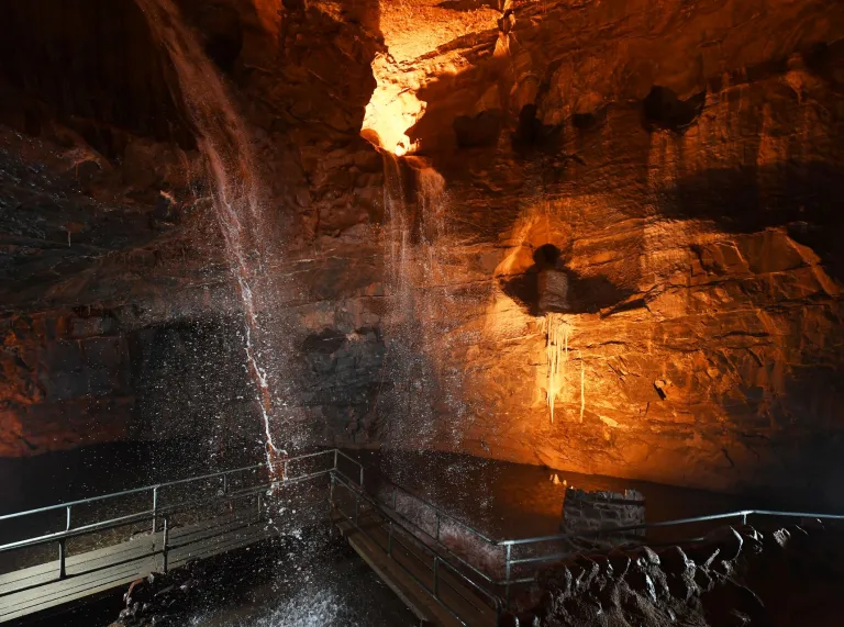 Dŵr yn llifo i lawr i bwll mewn ogof danddaearol, wedi'i oleuo.