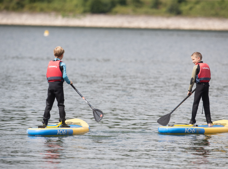 Dau o fechgyn yn padlfyrddio ar y llyn.