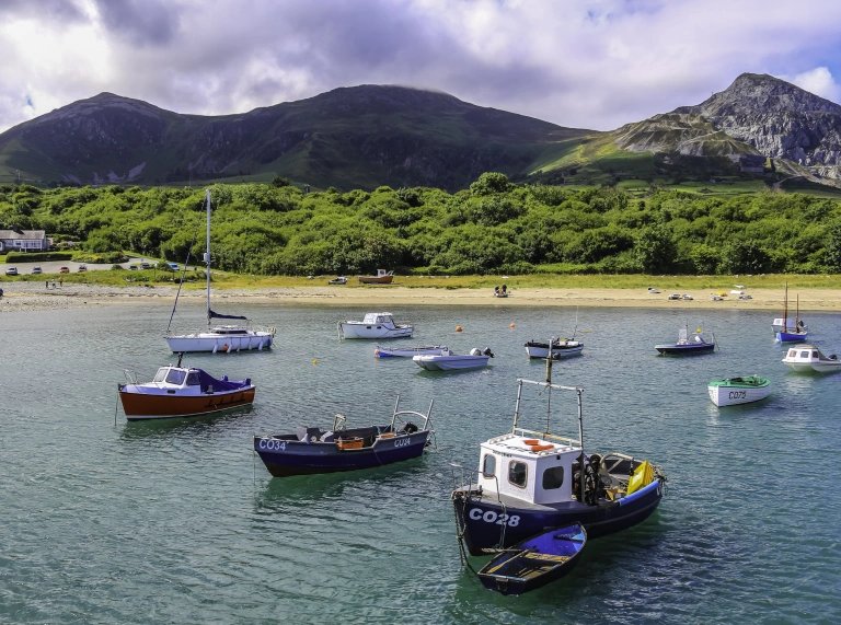 Cychod pysgota ar angor mewn harbwr gyda mynyddoedd yn y cefndir.