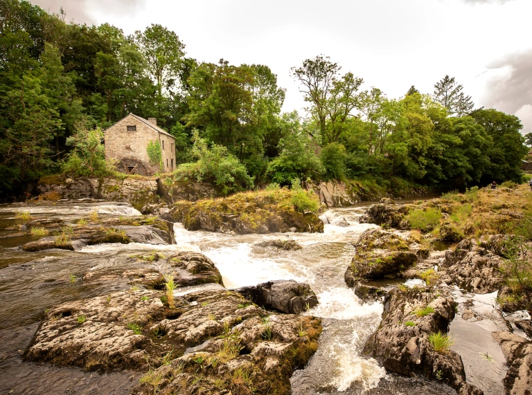 Rhaeadr gyda thŷ bychan yn y cefndir.