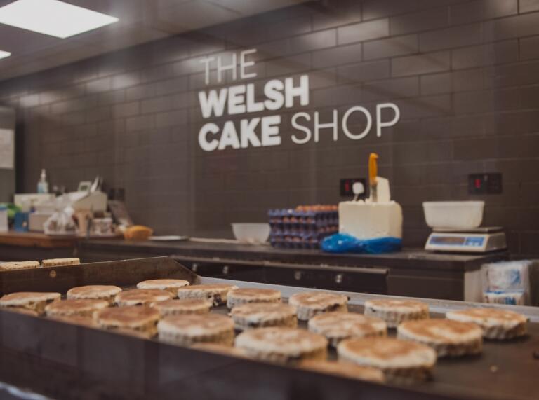 Stondin cacennau cri mewn marchnad gydag arwydd The Welsh Cake Shop.