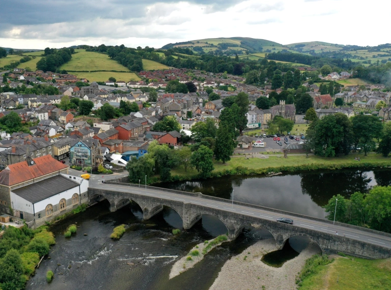 Golygfa o’r awyr o dref gyda phont gerrig fwaog dros afon lydan yn y blaendir.