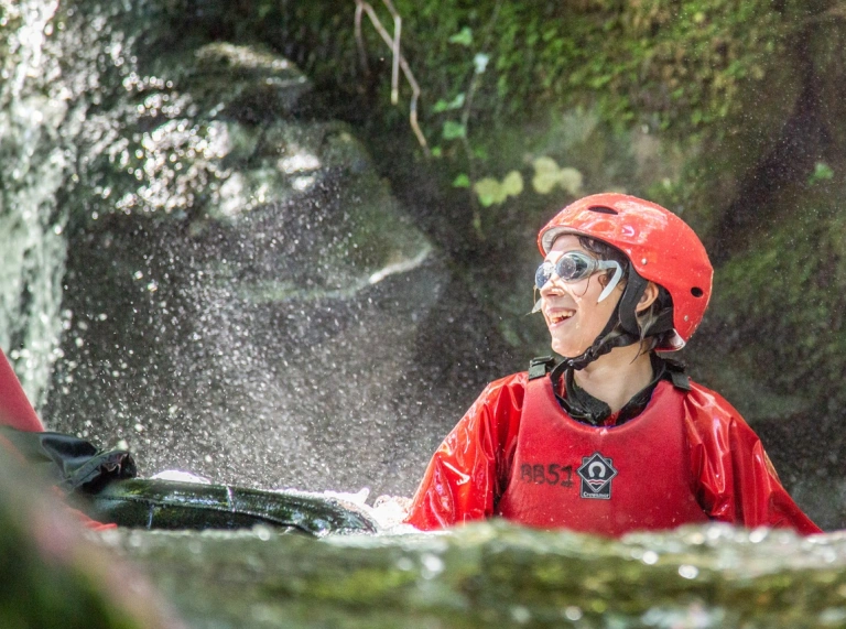 Close up of teens in helmets and wetsuits in a river having fun