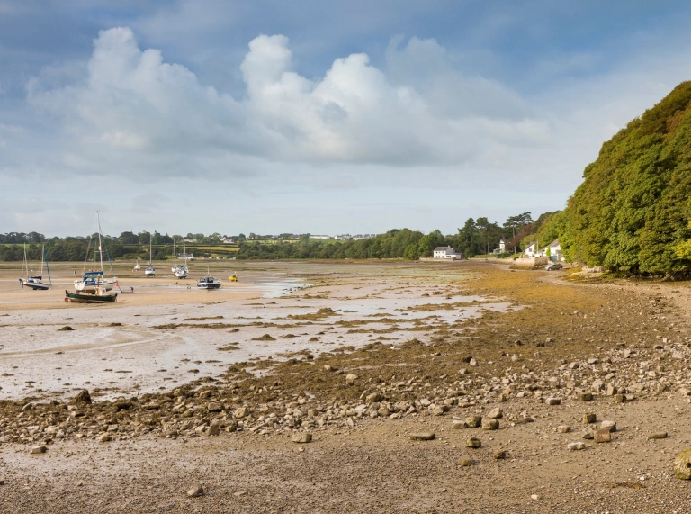 Traeth cerrig crynion gyda chychod wedi'u hangori yn y dŵr.