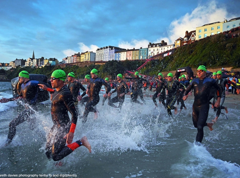Many swimmers wearing green caps running into the sea.