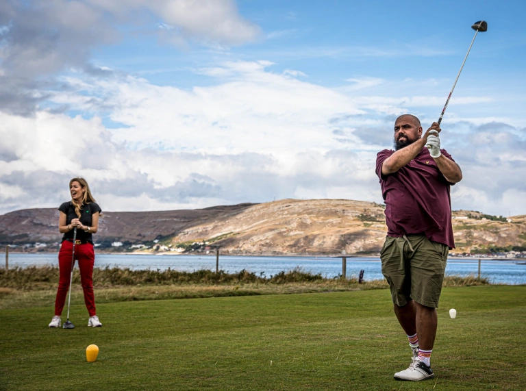 Dau golffiwr ar gwrs arfordirol.