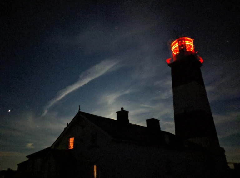 A lit lighthouse at night as seen from below.