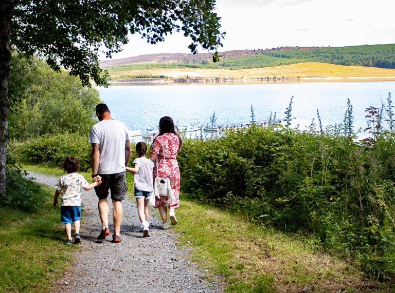 teulu yn cerdded ar hyd llwybr ger llyn.