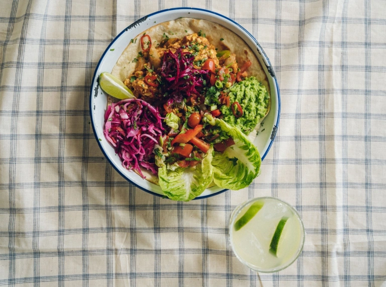 Salad lliwgar mewn powlen ar fwrdd gyda lliain bwrdd sgwariau glas a gwyn. Mae diod gyda leim wrth ei ochr.