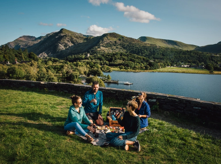 Teulu’n cael picnic gyda llyn yn y cefndir.