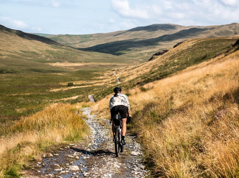 Beiciwr graean yn reidio ar drac graean mewn bryniau anghysbell.