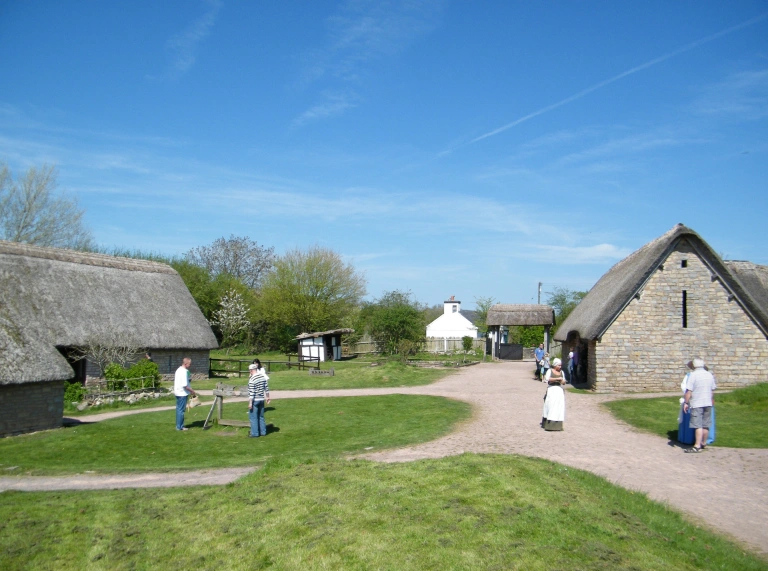 Y tu allan i adeiladau to gwellt ym Mhentref Cosmeston, gyda phobl yn crwydro.