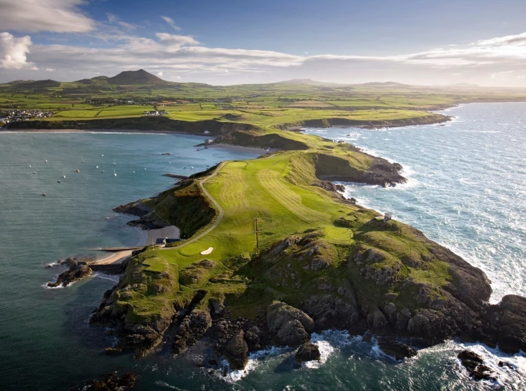 Golygfa o'r awyr o gwrs golff Nefyn ar benrhyn yn ymestyn tua'r tonnau.
