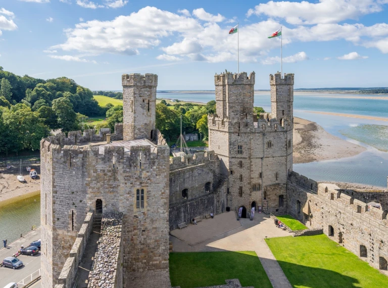 Castell Caernarfon gyda’r môr a choed yn y cefndir