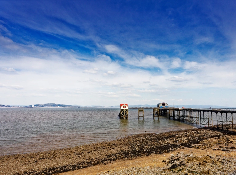 Pier yn mynd allan i'r môr gydag awyr las yn gefndir.