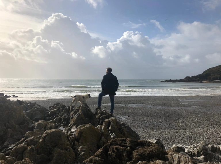 Dyn a chi yn sefyll ar graig, uwchben traeth caregog.