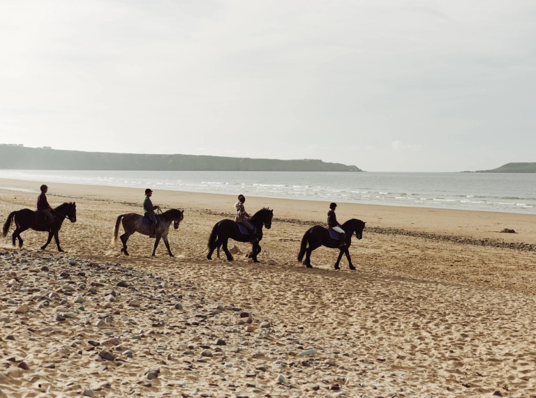 Pobl yn marchogaeth ar y traeth