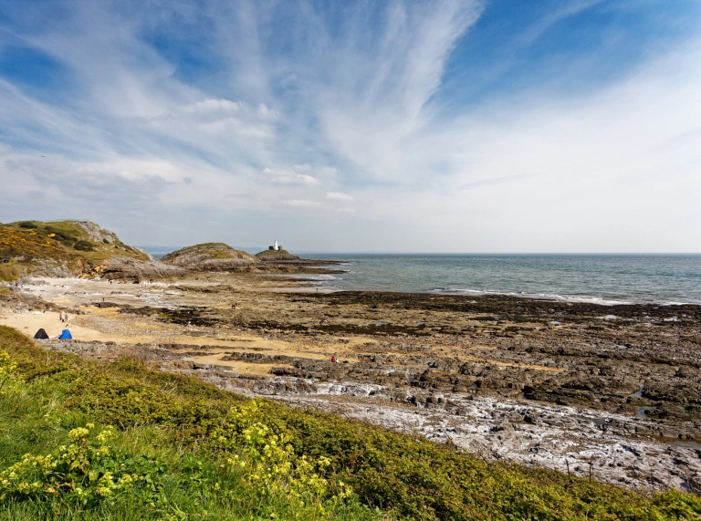 Traeth creigiog gyda goleudy ar un ochr.