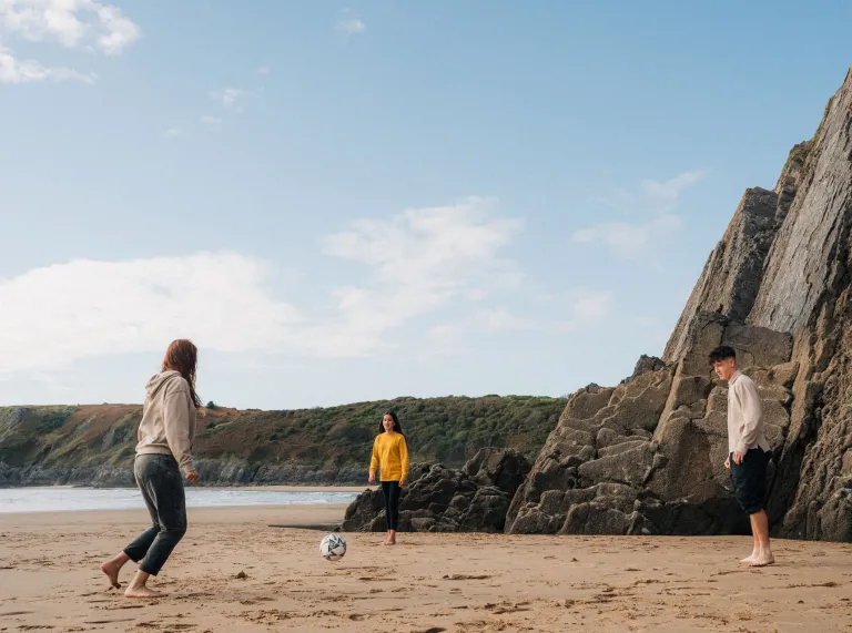 two teenage girls and boy playing football on sandy beach.
