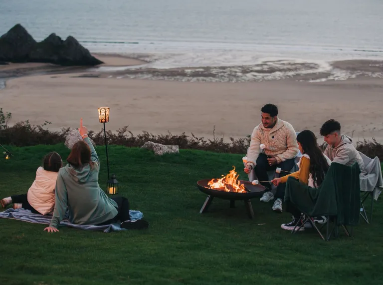family sat on cliff over looking the sea with camp fire.