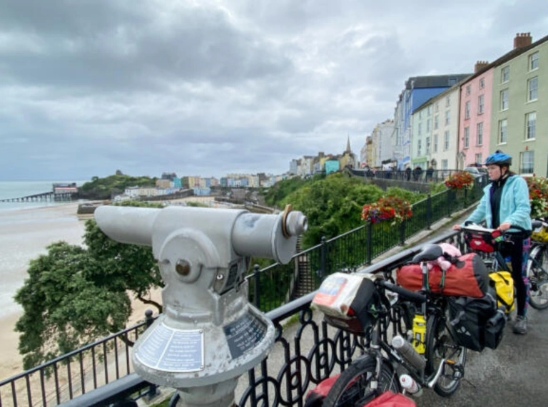 Beiciau a phobl yn sefyll ar hyd rheiliau yn edrych dros y traeth a'r môr.